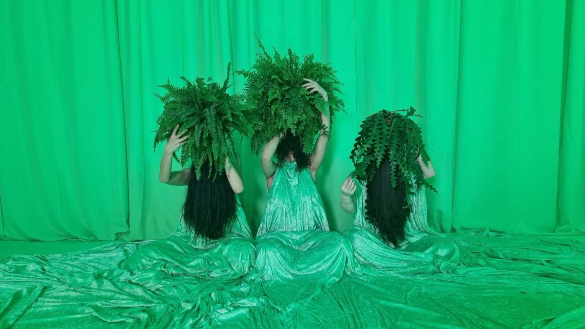Three figures lowering ferns in a green-lit installation at MOTHERBOARD